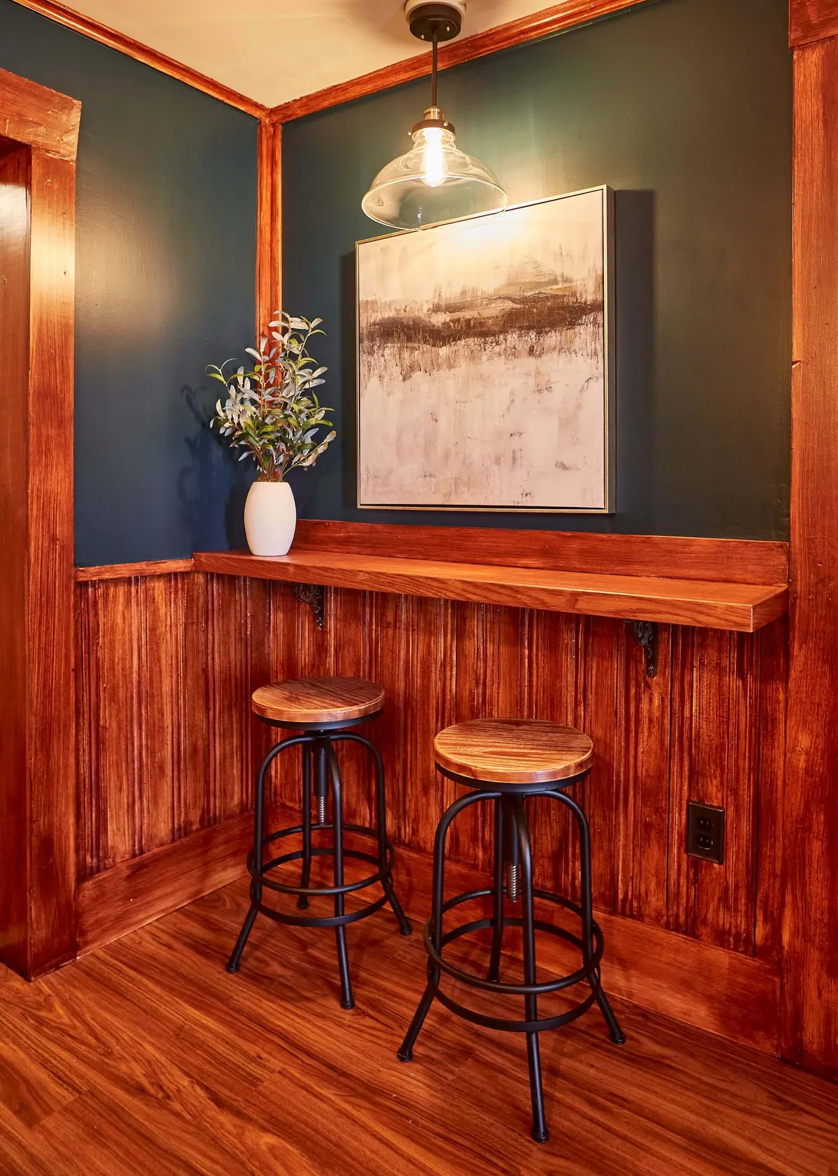 Here, a row of wooden bar stools sits at a counter, with decorative plants and abstract art providing a stylish, relaxed vibe. The setting encourages intimate conversations, shared meals, or even a quiet morning coffee, enhancing the homely ambiance of the breakfast nook.