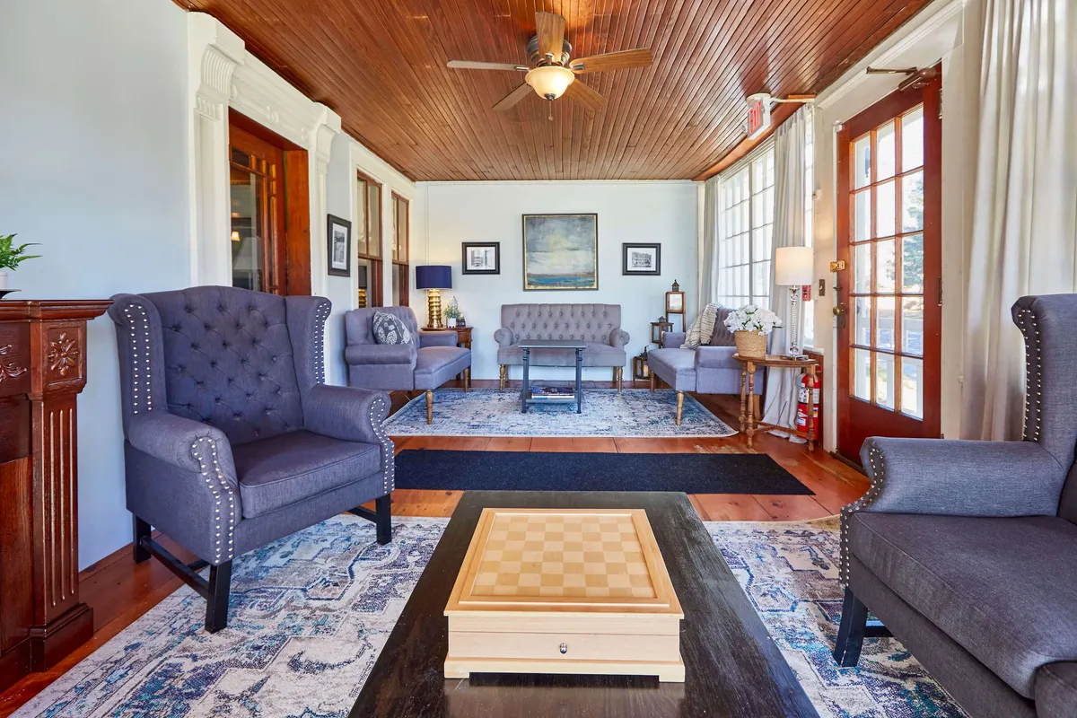 A welcoming interior scene centered around a chessboard table with two gray upholstered armchairs, wooden flooring, and attractive wall art. The setup invites both socializing and quiet games.