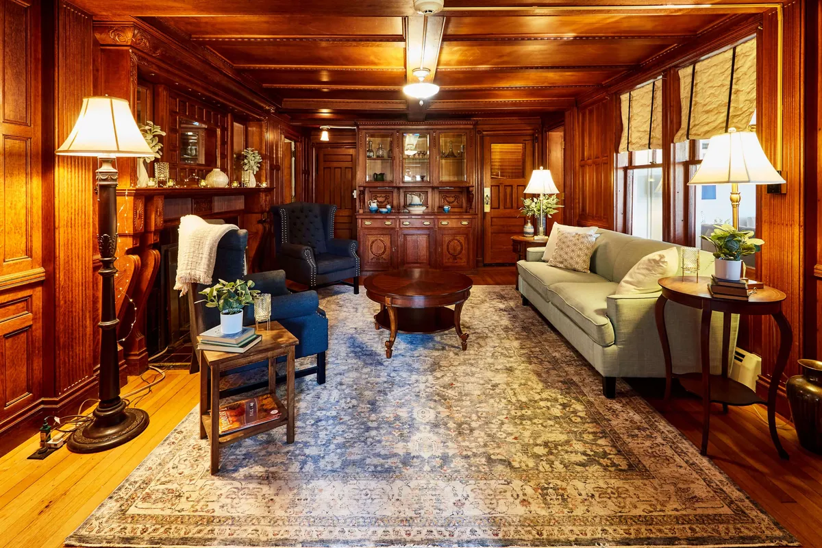 A warmly lit sitting room with elegant wooden paneling, a plush sofa, a central coffee table, and soft lighting from stylish lamps. The setting is cozy and inviting, ideal for gathering after a day outdoors. Decorative accents and layered textures evoke a sense of comfort and togetherness, making it perfect for socializing or relaxing.