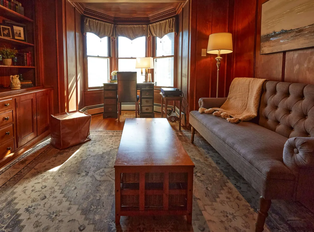 A sun-drenched living area with bay windows, a plush sofa, and decorative bookshelves, inviting relaxation and socializing. The abundance of natural light and views outside suggest a strong connection to the outdoors.