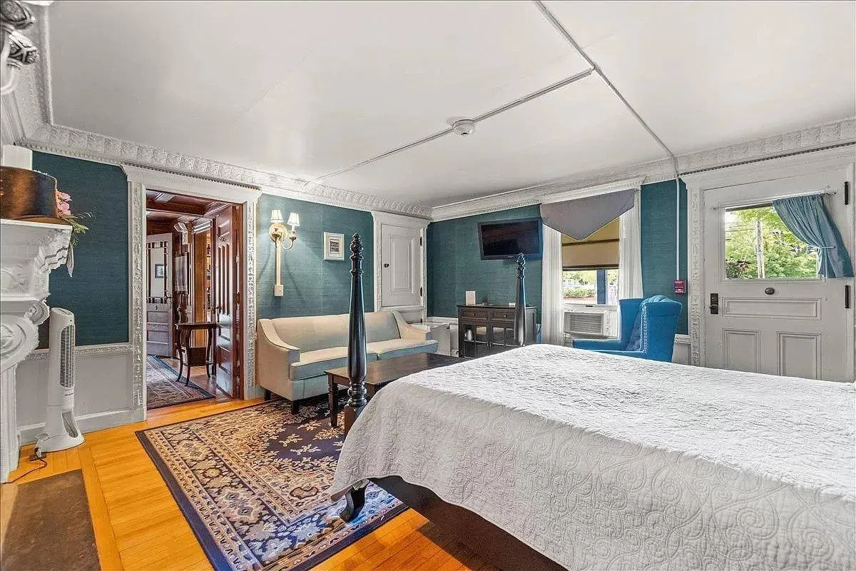 This image features a refined bedroom with a four-poster bed, a sofa, a decorative fireplace, television, and a window with views. The room is bathed in soft light, showcasing both comfort and elegance. The mix of historic architectural features and contemporary furnishings highlights the blend of old and new.