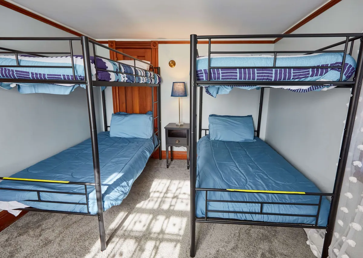 The image features a cozy bunk bed setup with a soft plush carpet and a nightstand with a lamp, set in a relaxed and communal atmosphere. The scene suggests a comfortable place for groups or families to gather, unwind, and bond after outdoor activities.