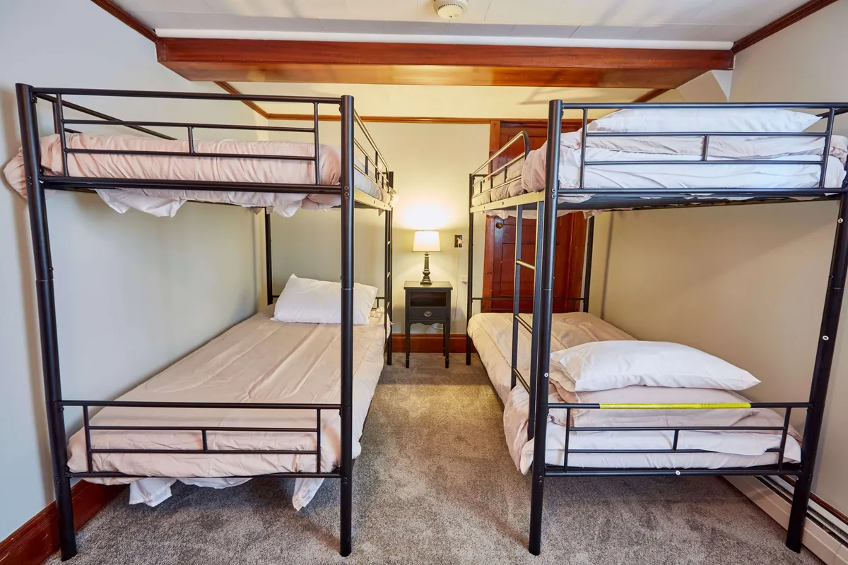 This image shows a room with bunk beds and a nightstand with a lamp, creating a cozy, communal environment ideal for groups to socialize and rest together. The space conveys a sense of shared adventure and bonding after a day outdoors.