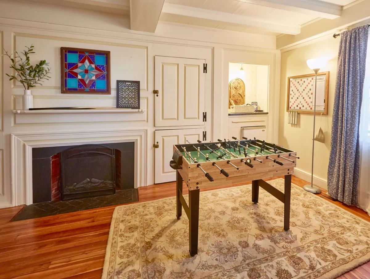 A playful and inviting gathering space featuring a foosball table, stained glass artwork, a fireplace, and a decorative shelf. The room is set for both active fun and relaxed moments, making it ideal for game nights and celebrations with friends or family.