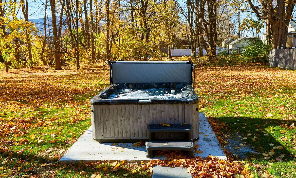 An outdoor hot tub set amidst autumn foliage, with a stone pathway and peaceful natural surroundings. The image emphasizes relaxation and rejuvenation in a scenic setting.